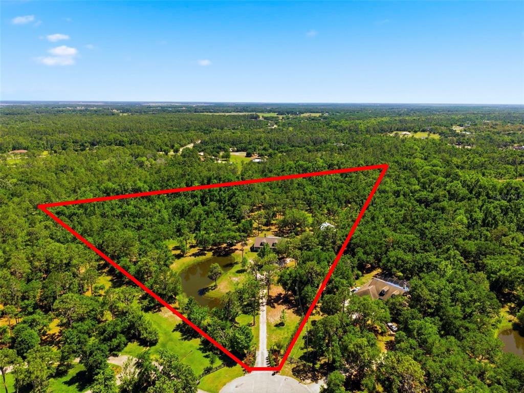 An aerial view shows a house and pond on a wooded lot outlined in red — 1115 410TH COURT E, MYAKKA CITY, FL