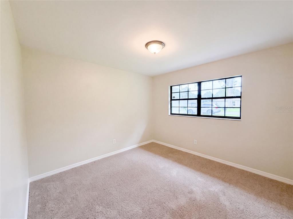 An empty bedroom features beige walls, tan carpeting, a ceiling light, and a grid-pane window — 6520 NW 61ST COURT, OCALA, FL