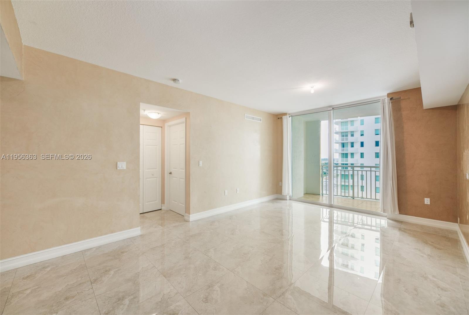 An empty living room features beige walls, large light-colored floor tiles, and a sliding glass door — 1755 E Hallandale Beach Blvd # 1408E, Hallandale Beach FL 33009, HALLANDALE BEACH, FL