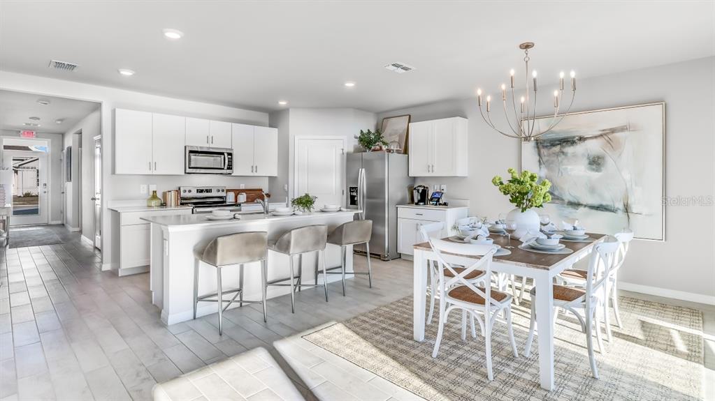 A bright, open-concept kitchen and dining area features white cabinetry, stainless appliances, and tile flooring — 1448 MABLETON DRIVE, PORT CHARLOTTE, FL