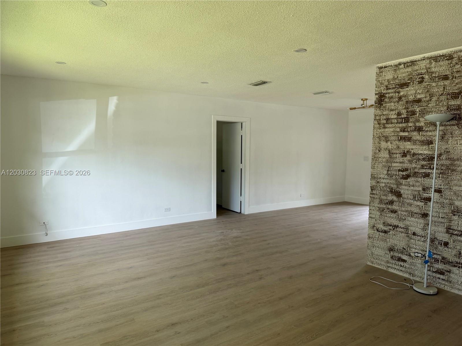 An empty room features light wood-look flooring, white walls, recessed lighting, and a brick accent wall — 7220 NW 7th St, Plantation FL 33317, PLANTATION, FL