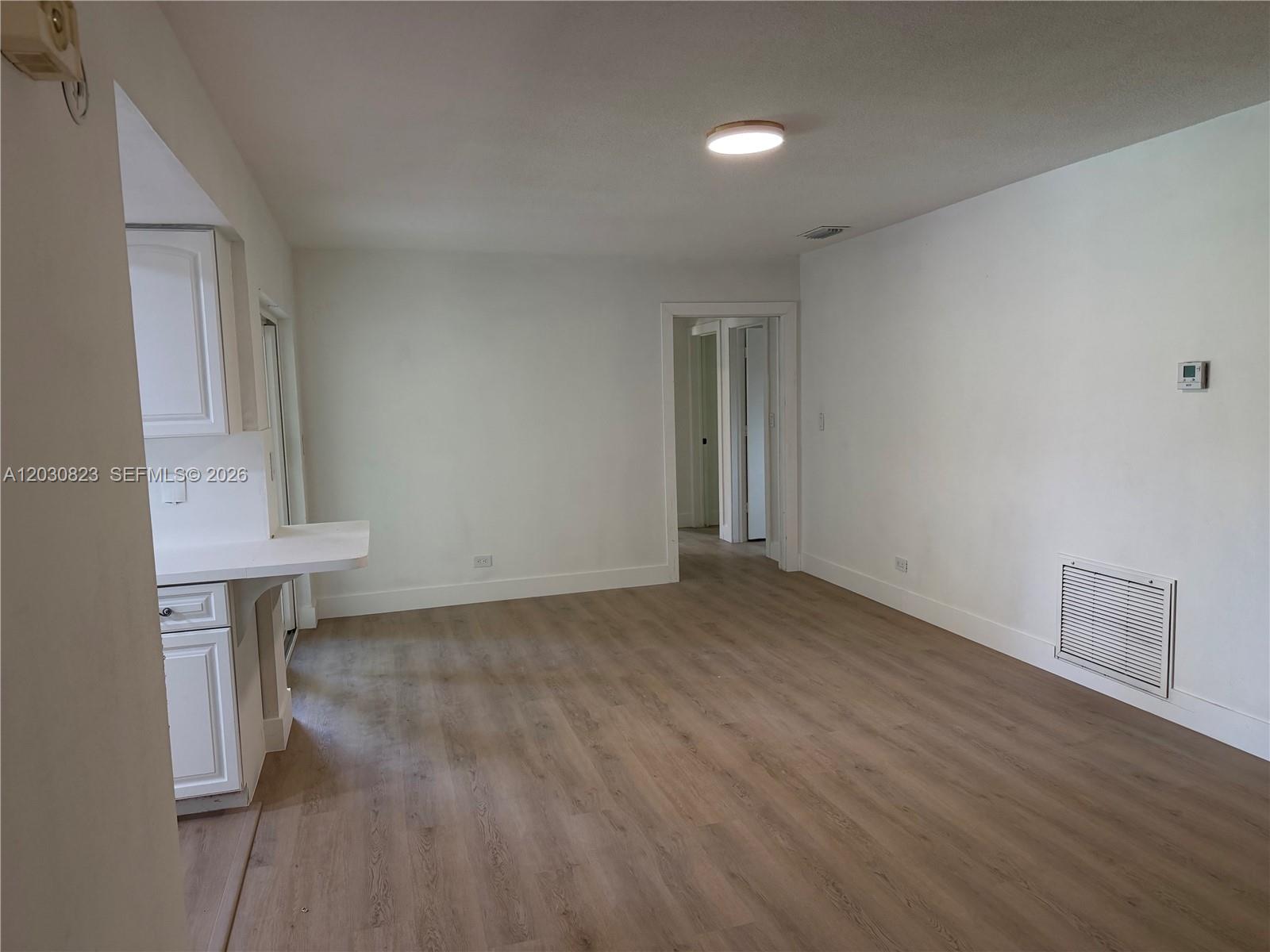 An empty room with light wood-look flooring, white walls, and a kitchen counter extension — 7220 NW 7th St, Plantation FL 33317, PLANTATION, FL