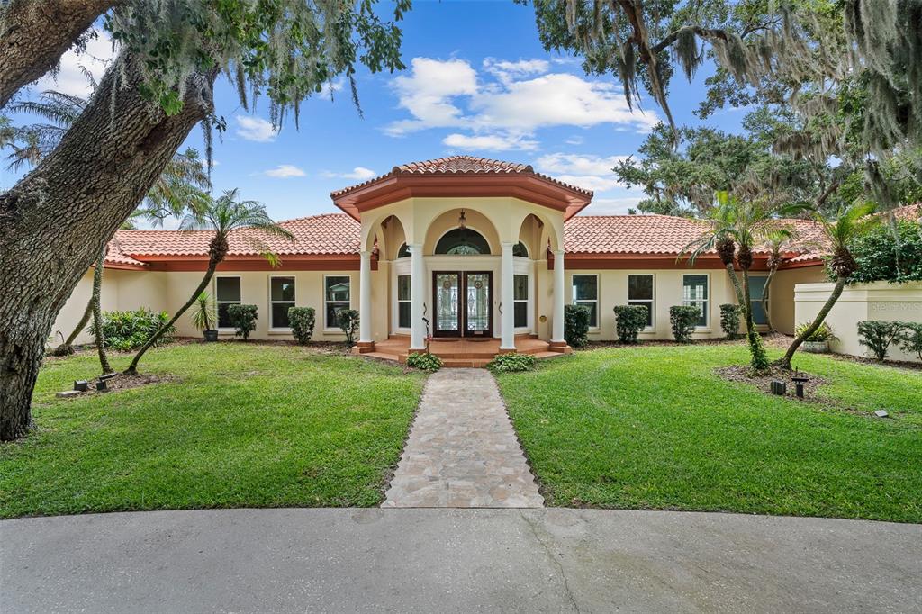 A single-story house with a tiled roof and a central arched entryway with white columns — 1412 MOSSWOOD DR, LEESBURG, FL