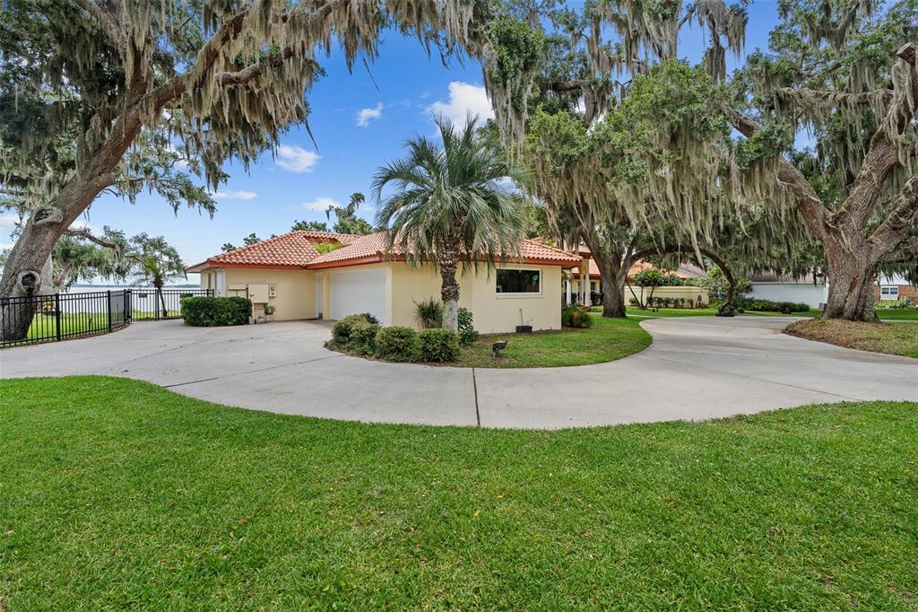 A single-story house with a tile roof and circular driveway sits under large oak trees — 1412 MOSSWOOD DR, LEESBURG, FL