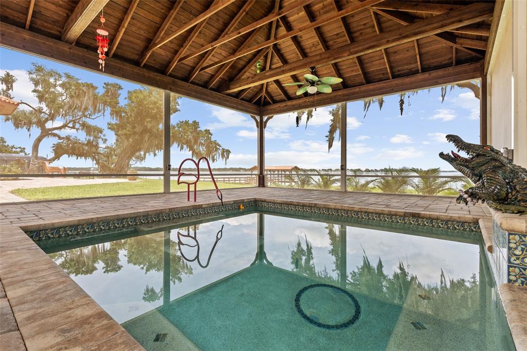 A covered pool enclosure overlooks a lake with a decorative alligator statue on the deck — 1412 MOSSWOOD DR, LEESBURG, FL