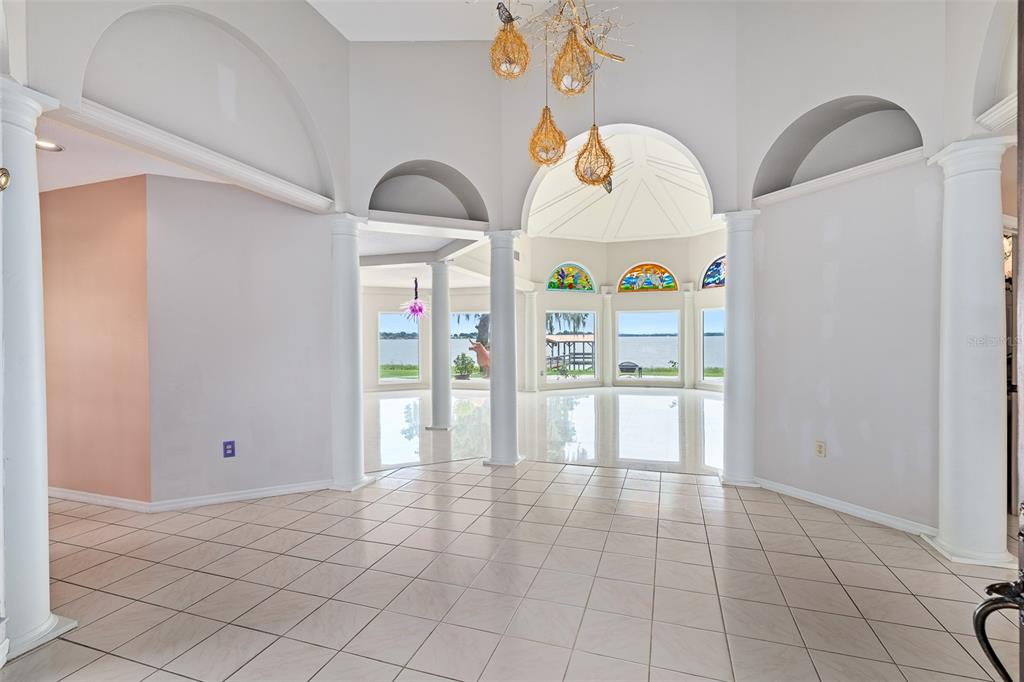 A bright, open-concept room features white tiled floors, arched architectural details, columns, and lake views — 1412 MOSSWOOD DR, LEESBURG, FL