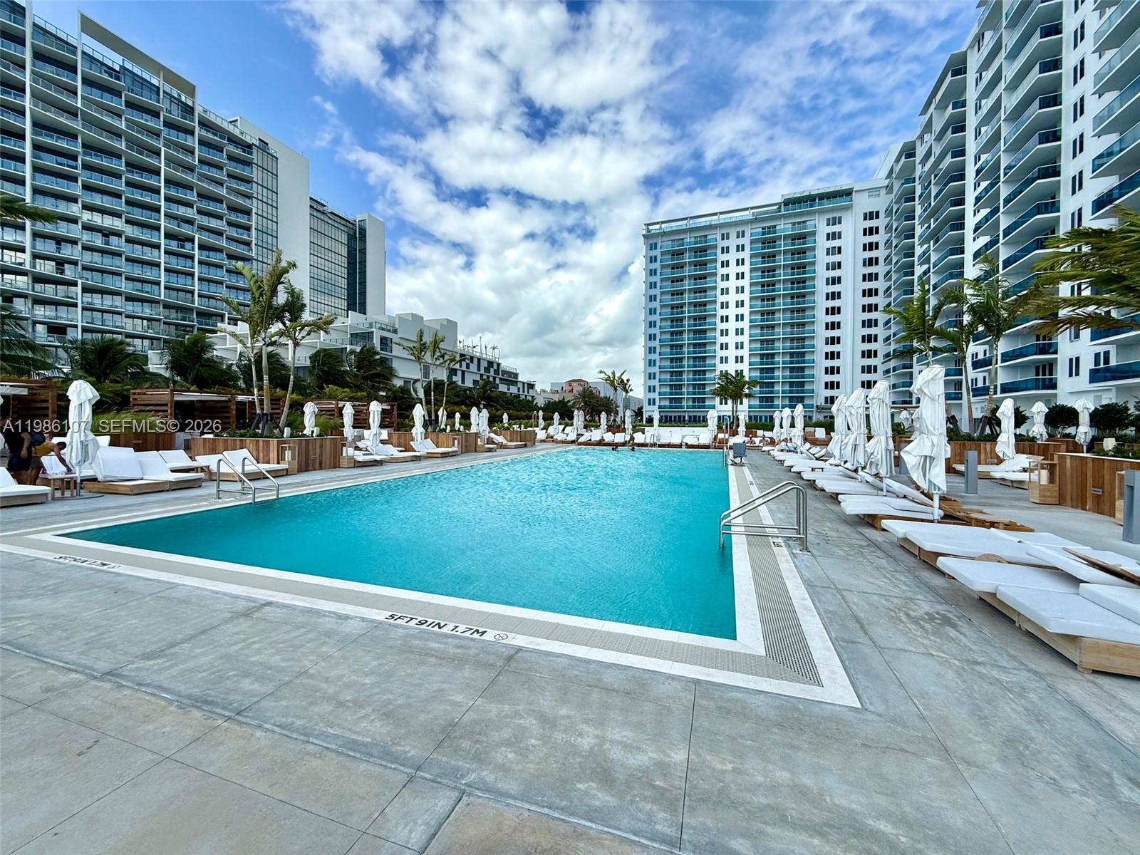 A large outdoor swimming pool is surrounded by lounge chairs and tall residential buildings — 2301 Collins Ave # 931, Miami Beach FL 33139, MIAMI BEACH, FL