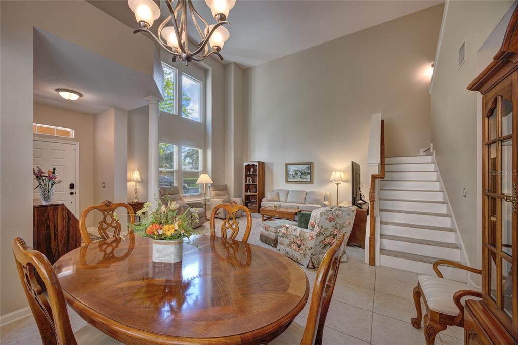 A dining area with a wooden table opens into a high-ceilinged living room with stairs — 901 WYNBROOK LANE, DELAND, FL