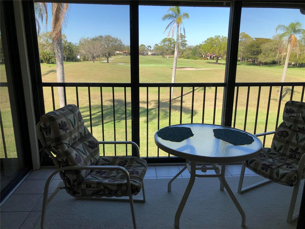A screened-in balcony features a small table and two chairs overlooking a golf course — 6211 TIMBER LAKE DRIVE UNIT B4, SARASOTA, FL
