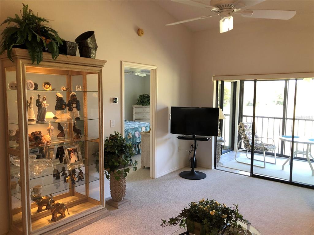A living room features a glass display cabinet, a television on a stand, and a balcony — 6211 TIMBER LAKE DRIVE UNIT B4, SARASOTA, FL