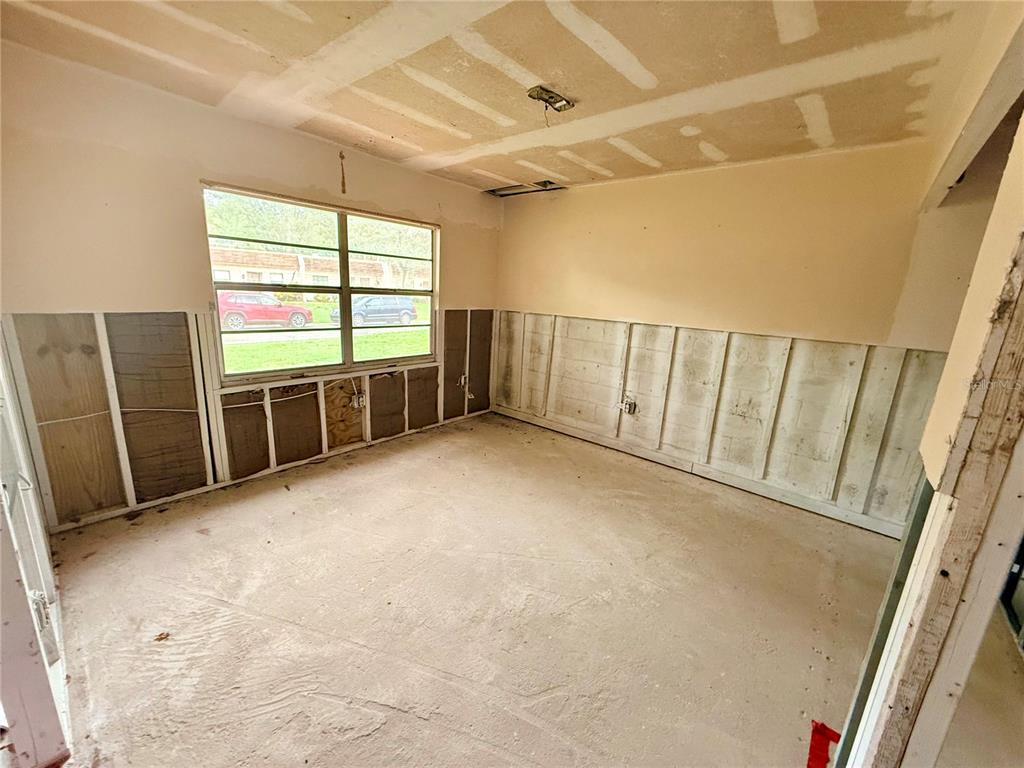 An unfinished room features exposed wall studs, bare concrete flooring, and a window overlooking cars — 1380 MISSION CIRCLE UNIT 44-C, CLEARWATER, FL