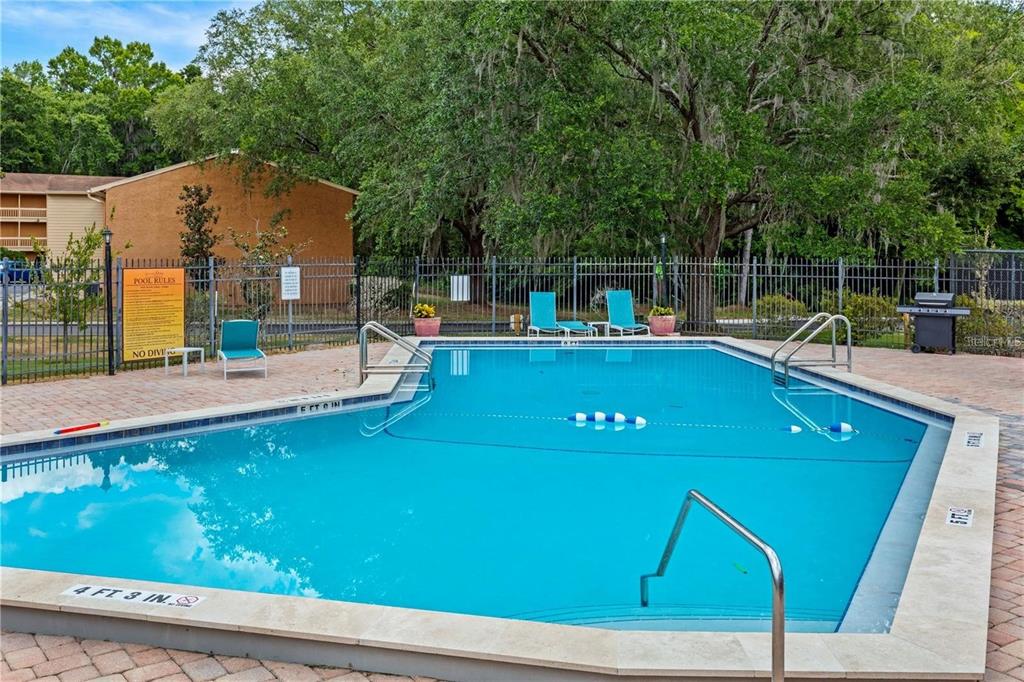 A rectangular outdoor swimming pool is surrounded by a brick patio and a metal fence — 1810 NW 23RD BOULEVARD UNIT 202, GAINESVILLE, FL