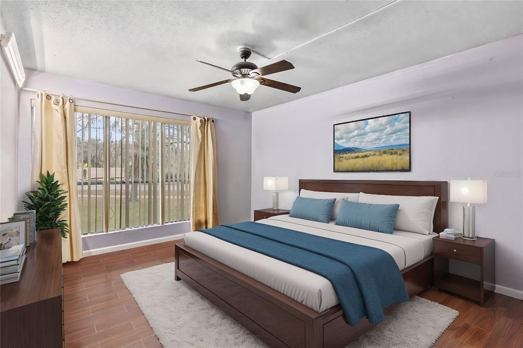 A bedroom features a wooden bed frame, blue bedding, a ceiling fan, and large windows — 1810 NW 23RD BOULEVARD UNIT 202, GAINESVILLE, FL