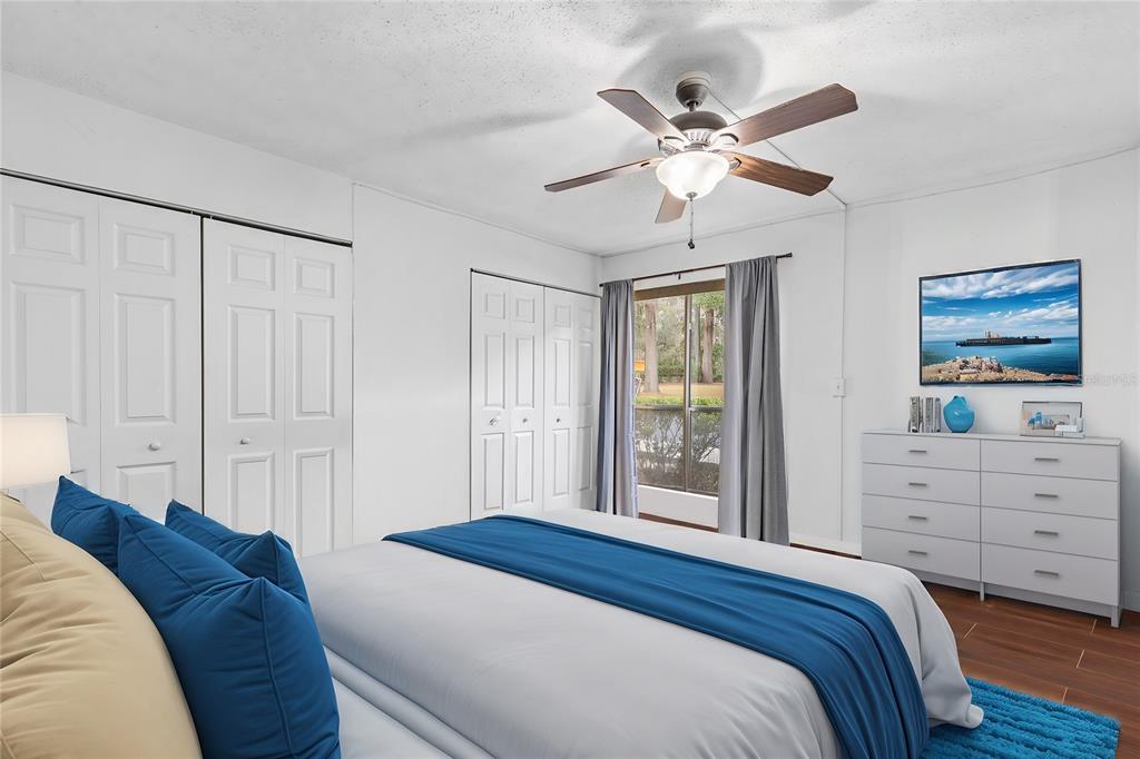 A bedroom features a bed with blue bedding, white closets, a ceiling fan, and dresser — 1810 NW 23RD BOULEVARD UNIT 202, GAINESVILLE, FL