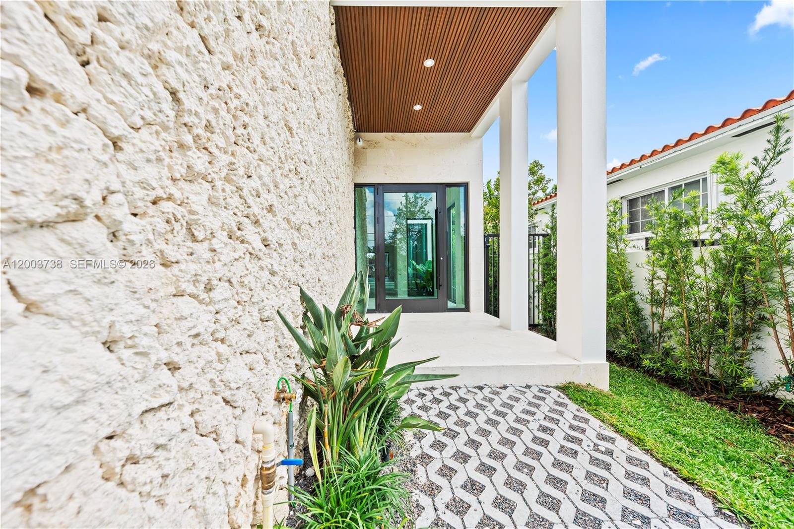 A modern entryway features a textured stone wall, a wood-paneled ceiling, and a paved walkway — 3320 SW 23rd St, Miami FL 33145, MIAMI, FL