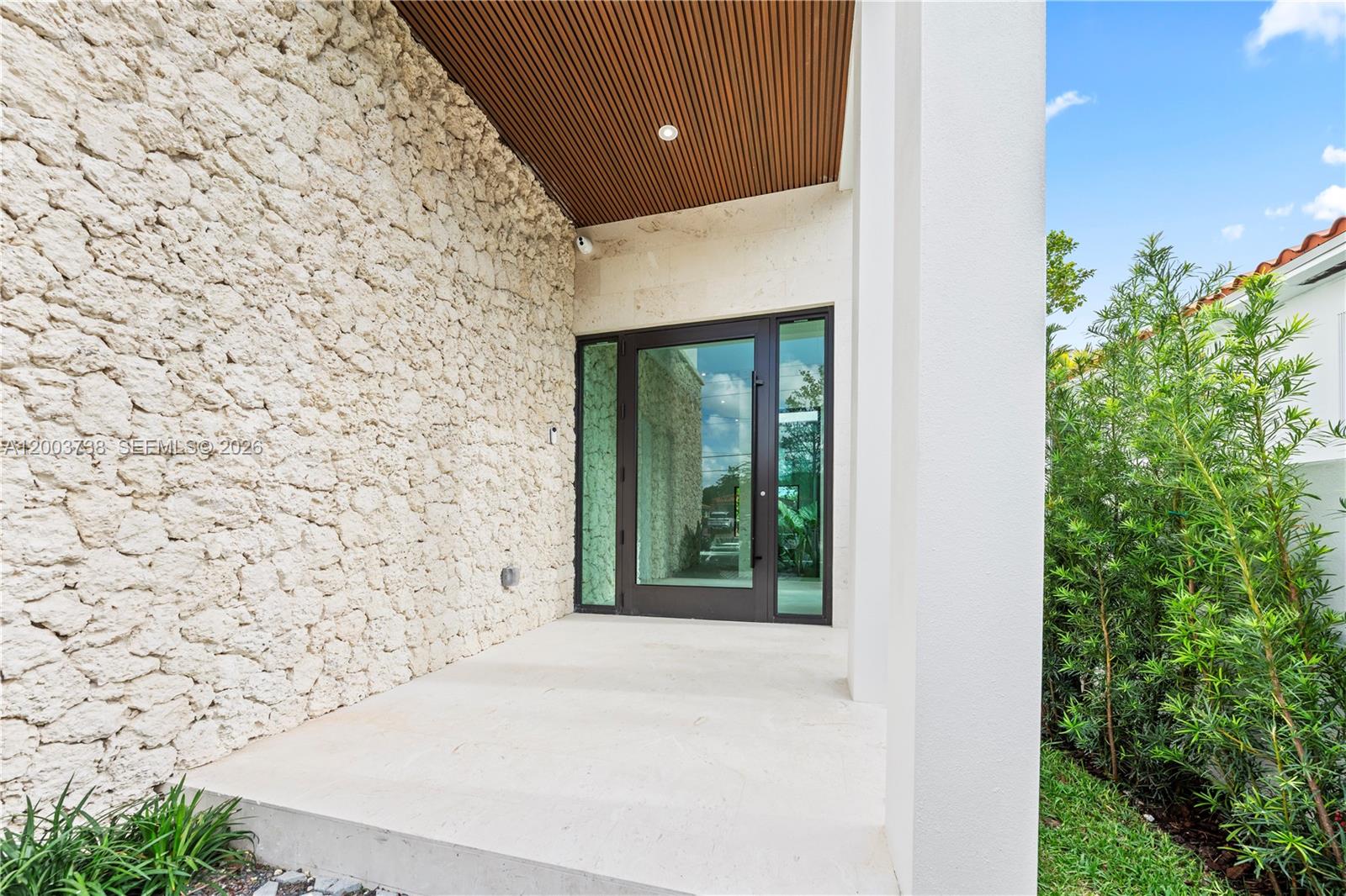 A modern entryway features a textured stone wall, a glass door, and a slatted wood ceiling — 3320 SW 23rd St, Miami FL 33145, MIAMI, FL