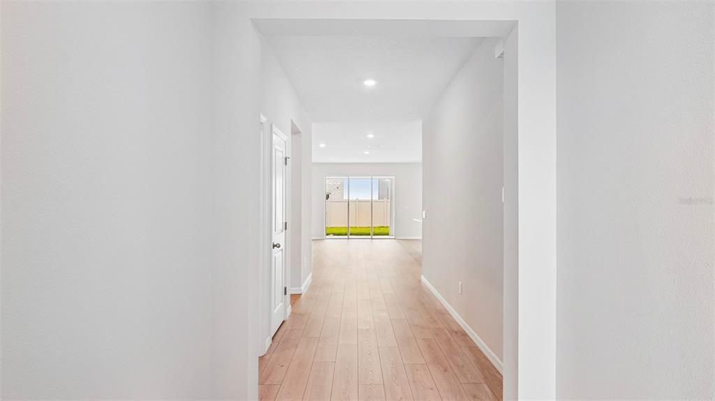 A hallway with light wood-look flooring leads toward a glass sliding door viewing a backyard — 2032 VANDALIA PLACE, PARRISH, FL