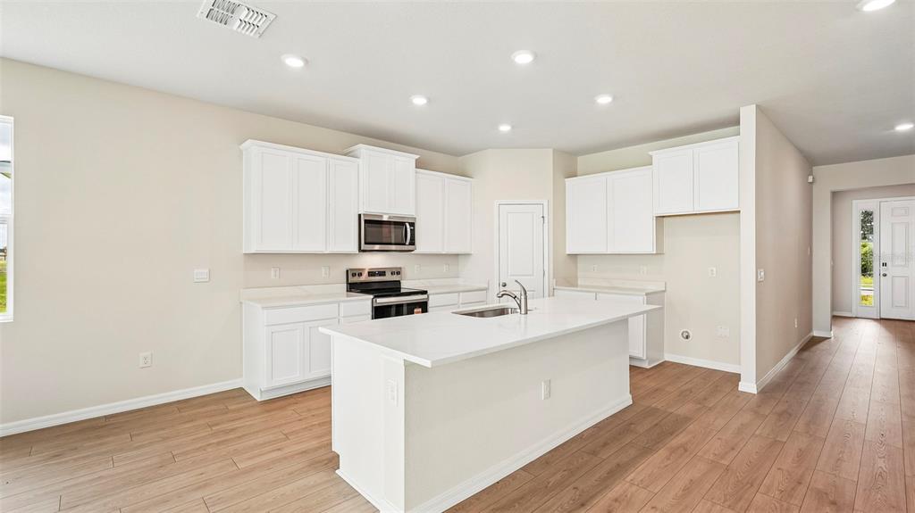 A modern kitchen features white cabinets, a central island, and light wood-look flooring — 2032 VANDALIA PLACE, PARRISH, FL