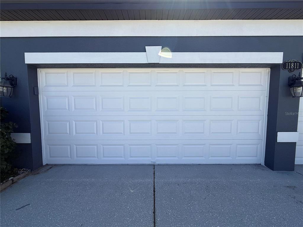 A white sectional garage door is set into a dark gray exterior wall — 11811 HARPSWELL DRIVE, RIVERVIEW, FL
