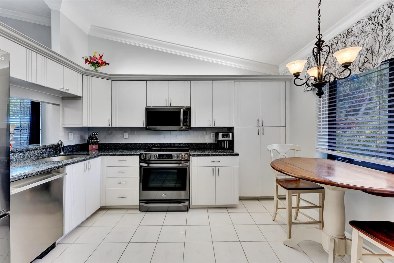 A kitchen features white cabinets, granite countertops, stainless steel appliances, and a small dining area — 8379 Boca Glades Boulevard E, Boca Raton FL 33434, BOCA RATON, FL
