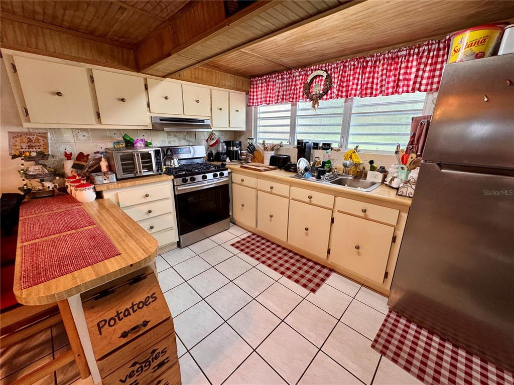 A kitchen features light-colored cabinets, a stainless steel stove, and a red checkered valance — 14 CHISTIAN BELÉN, AIBONITO, PR