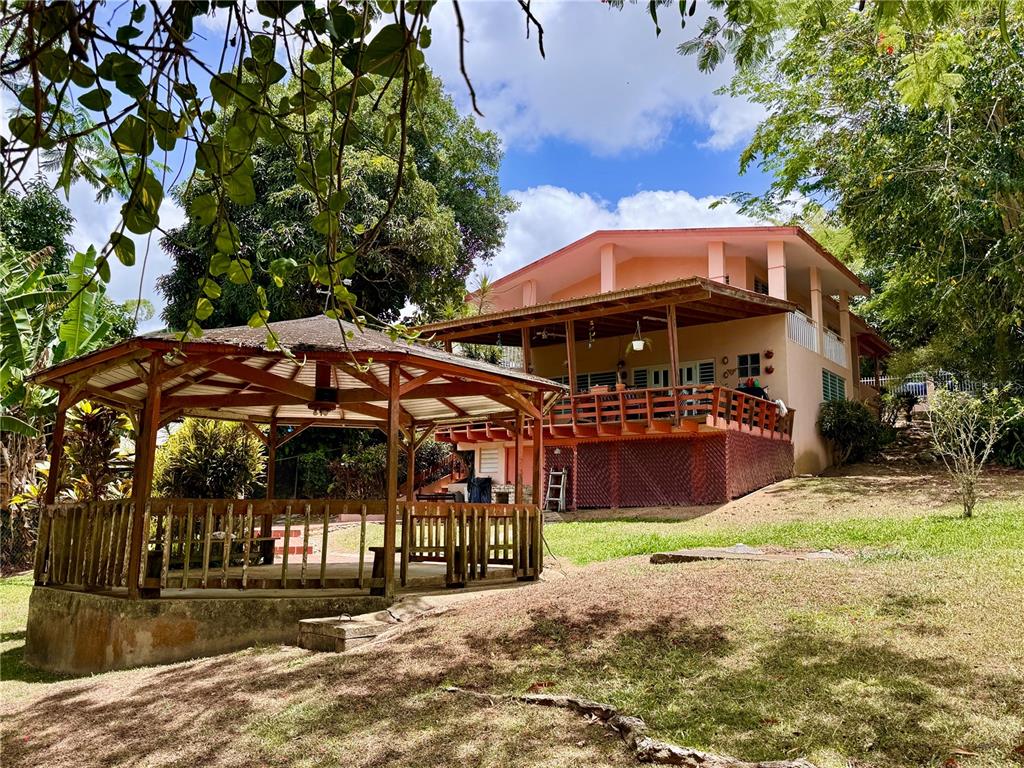 A wooden gazebo stands in a grassy yard in front of a two-story peach-colored house — 14 CHISTIAN BELÉN, AIBONITO, PR