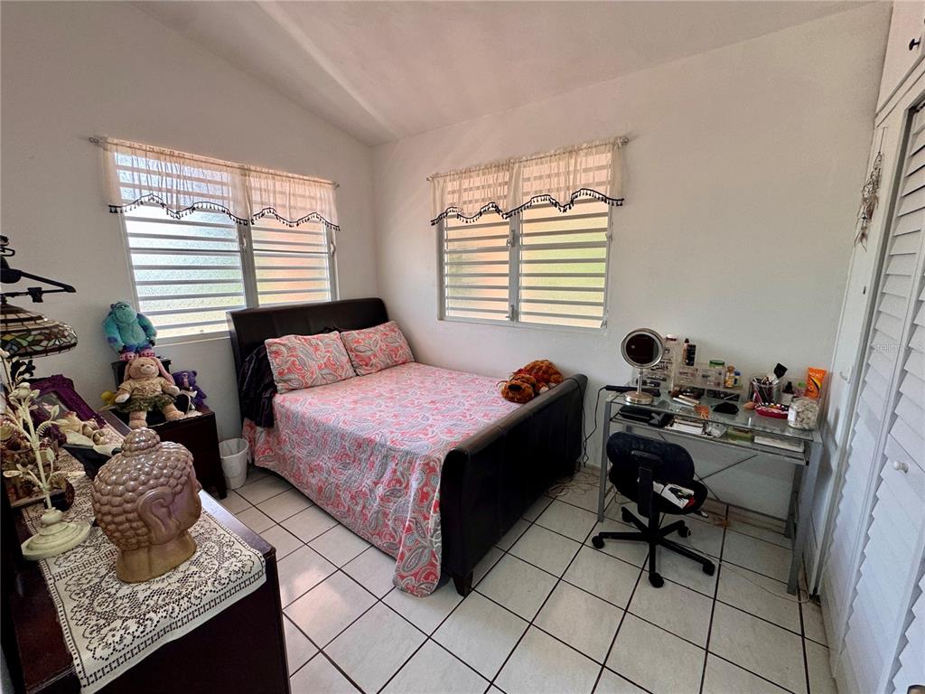 A bedroom features a bed with a patterned quilt, a desk, and white tiled floors — 14 CHISTIAN BELÉN, AIBONITO, PR