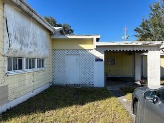 A yellow house exterior features a white lattice entryway, a carport, and a metal awning — 602 W Midway Road, Fort Pierce FL 34982, FORT PIERCE, FL