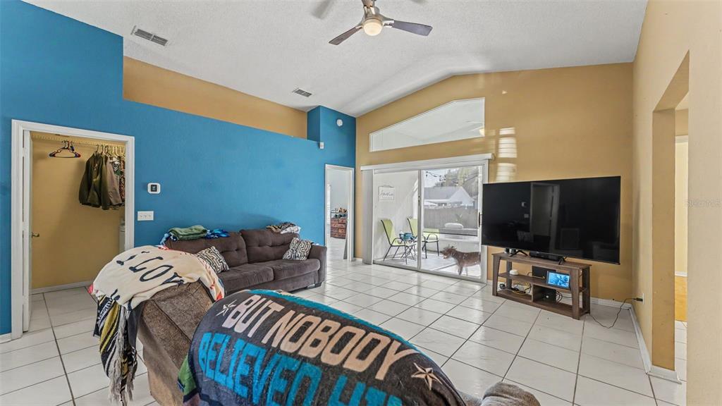 A living room features a blue accent wall, tile flooring, a vaulted ceiling, and sliding doors — 7493 BRIARBAY LOOP, LAKELAND, FL