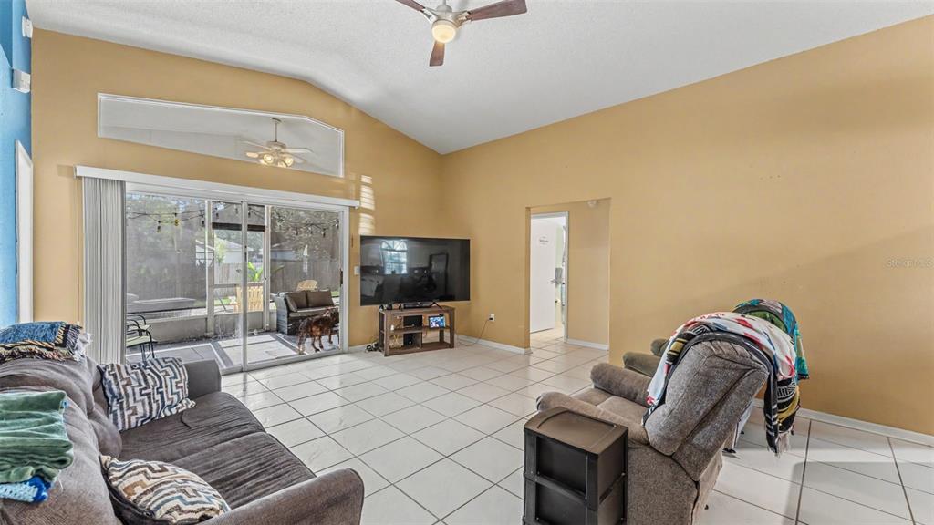 A living room with vaulted ceilings, tile floors, a television, and a sliding glass door — 7493 BRIARBAY LOOP, LAKELAND, FL