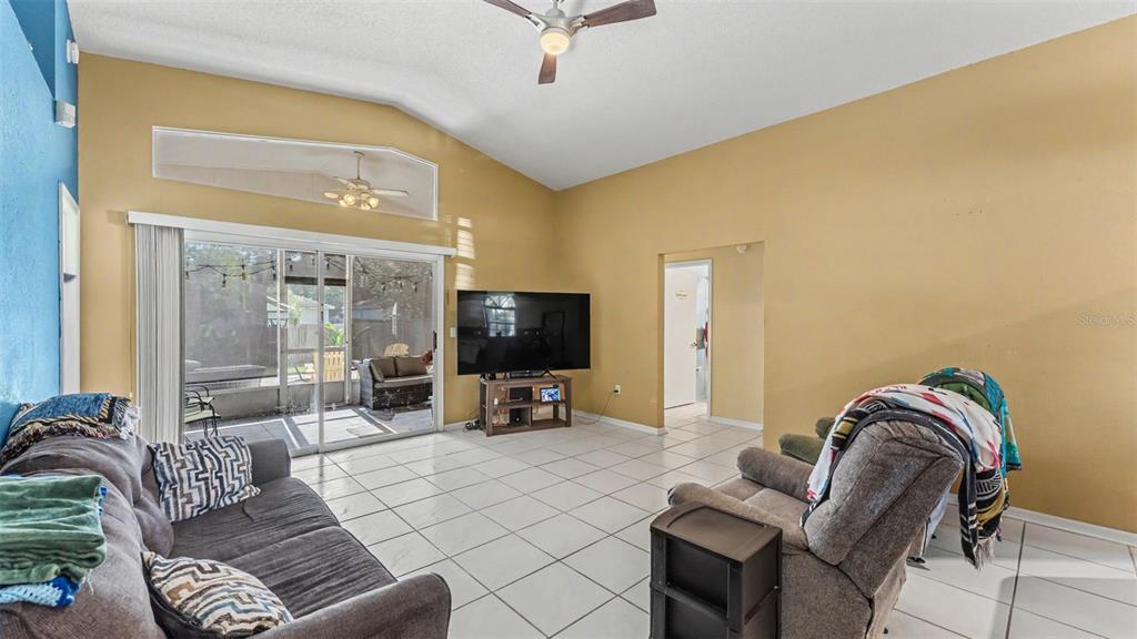 A living room with vaulted ceilings, tile floors, a television, and a sliding glass door — 7493 BRIARBAY LOOP, LAKELAND, FL