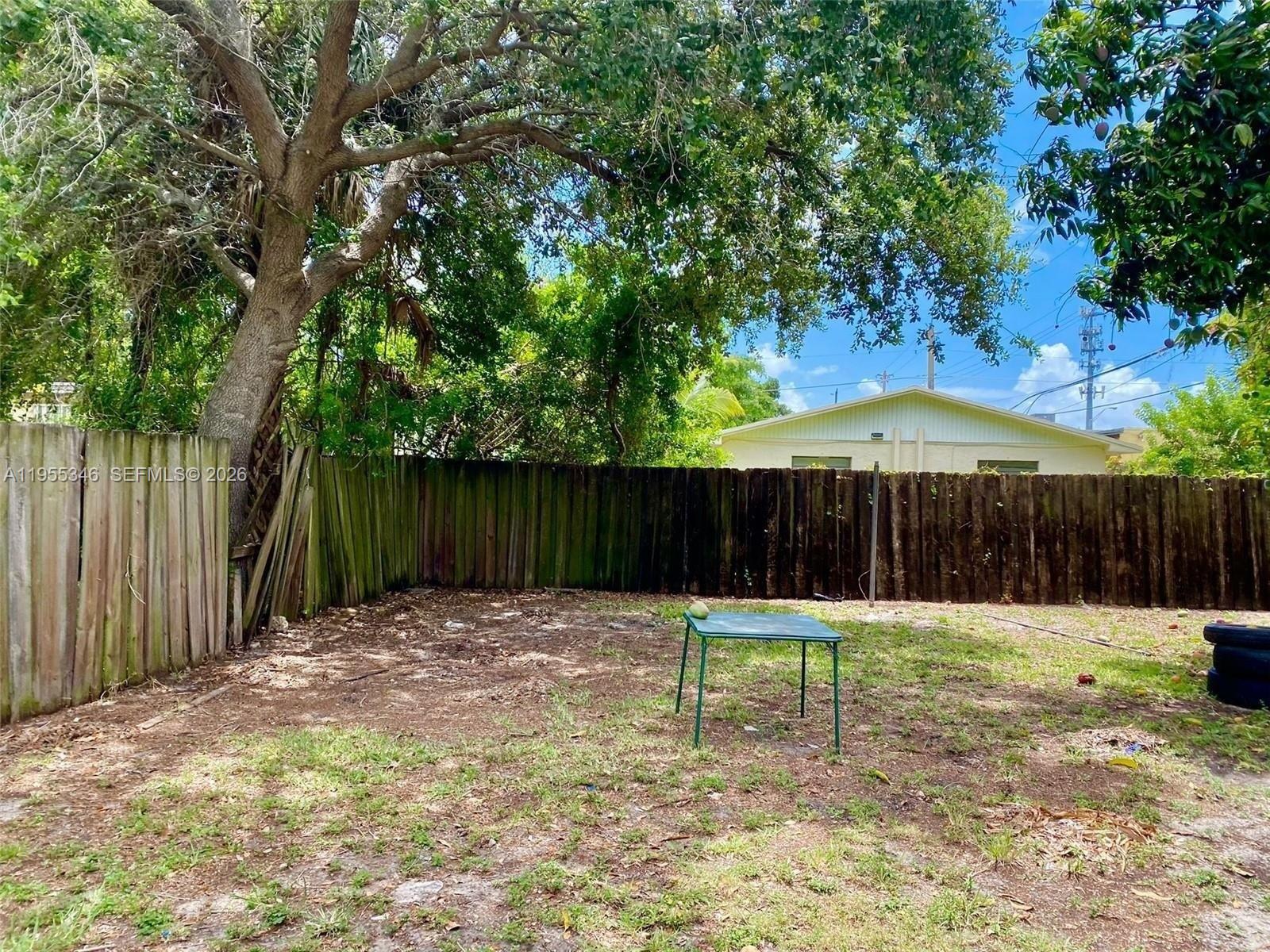 A backyard features a wooden fence, a small green table, and a large tree — 5411 NW 6th Ave, Miami FL 33127, MIAMI, FL