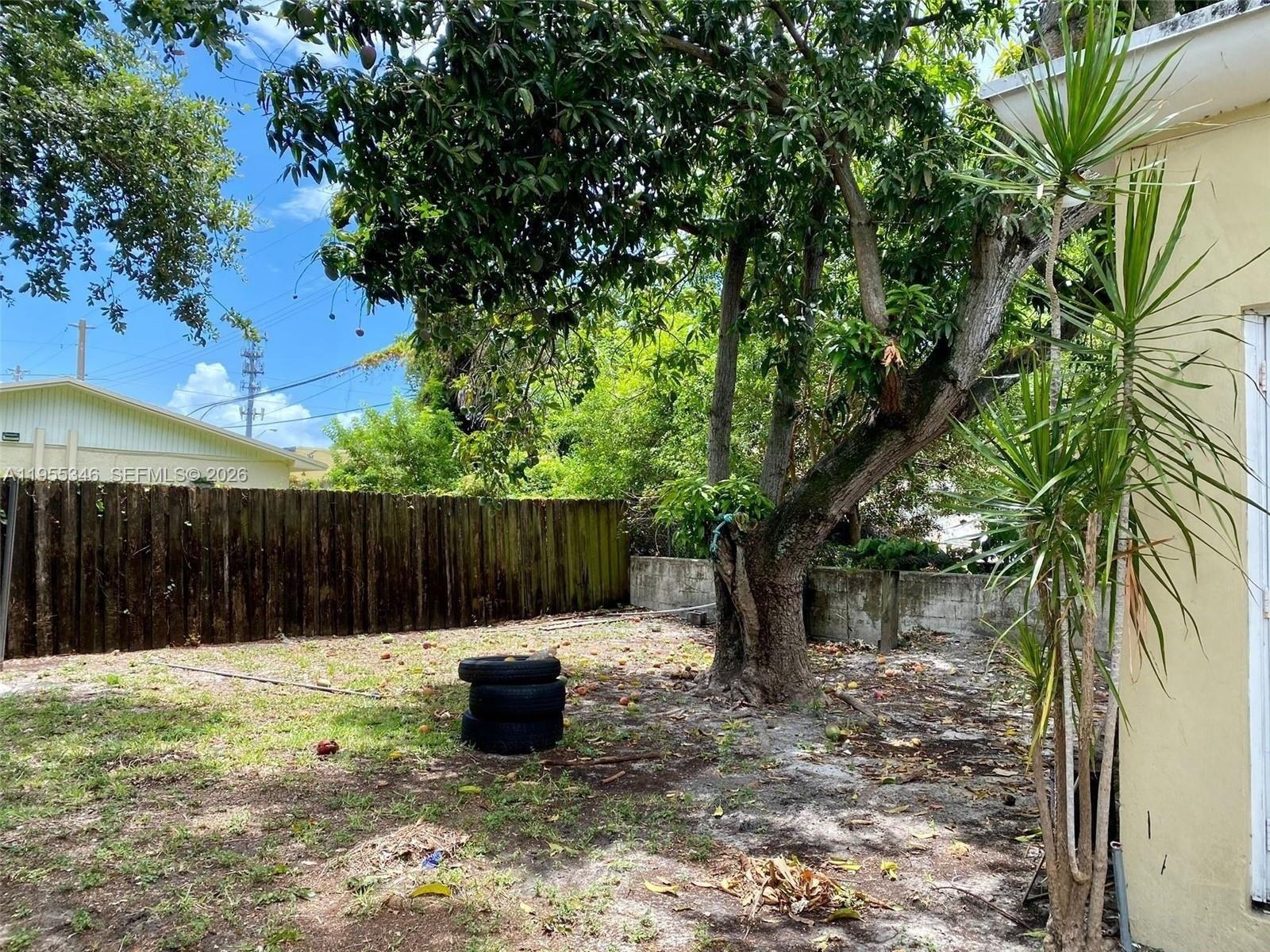 A backyard features a large tree, a wooden fence, and a stack of tires — 5411 NW 6th Ave, Miami FL 33127, MIAMI, FL