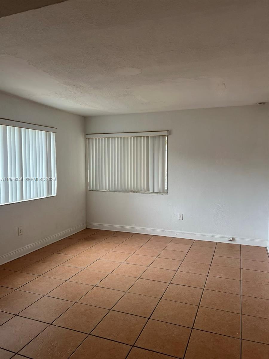 An empty room features white walls, vertical blinds on two windows, and brown tile flooring — 5411 NW 6th Ave, Miami FL 33127, MIAMI, FL