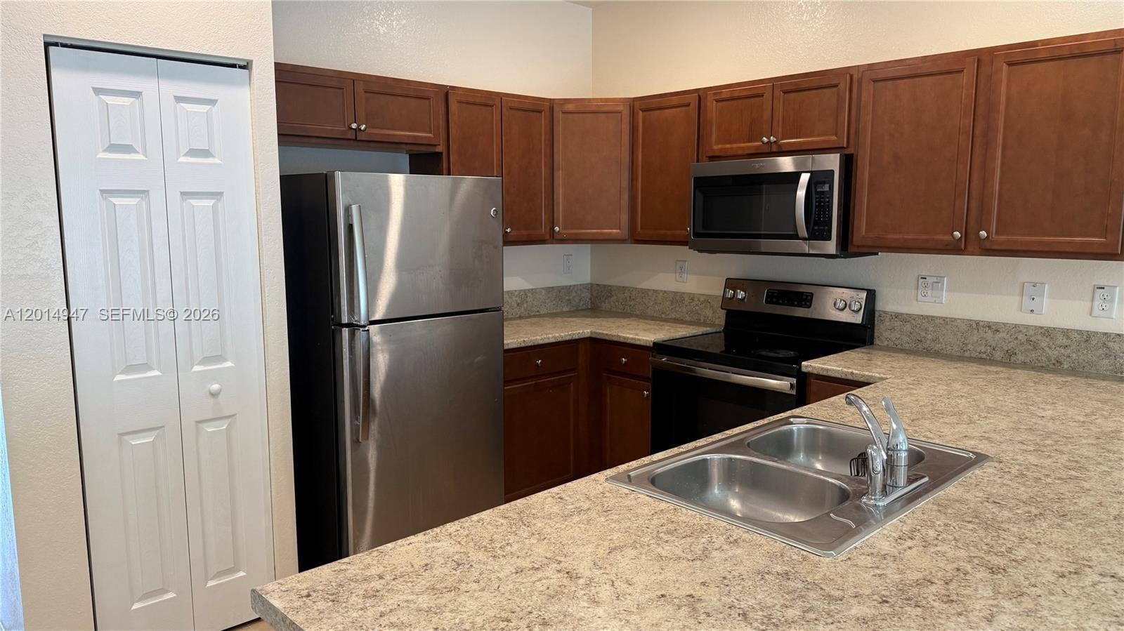 A kitchen features brown cabinets, stainless steel appliances, and a double-basin sink on the counter — 9213 W 33rd Way, Hialeah FL 33018, HIALEAH, FL