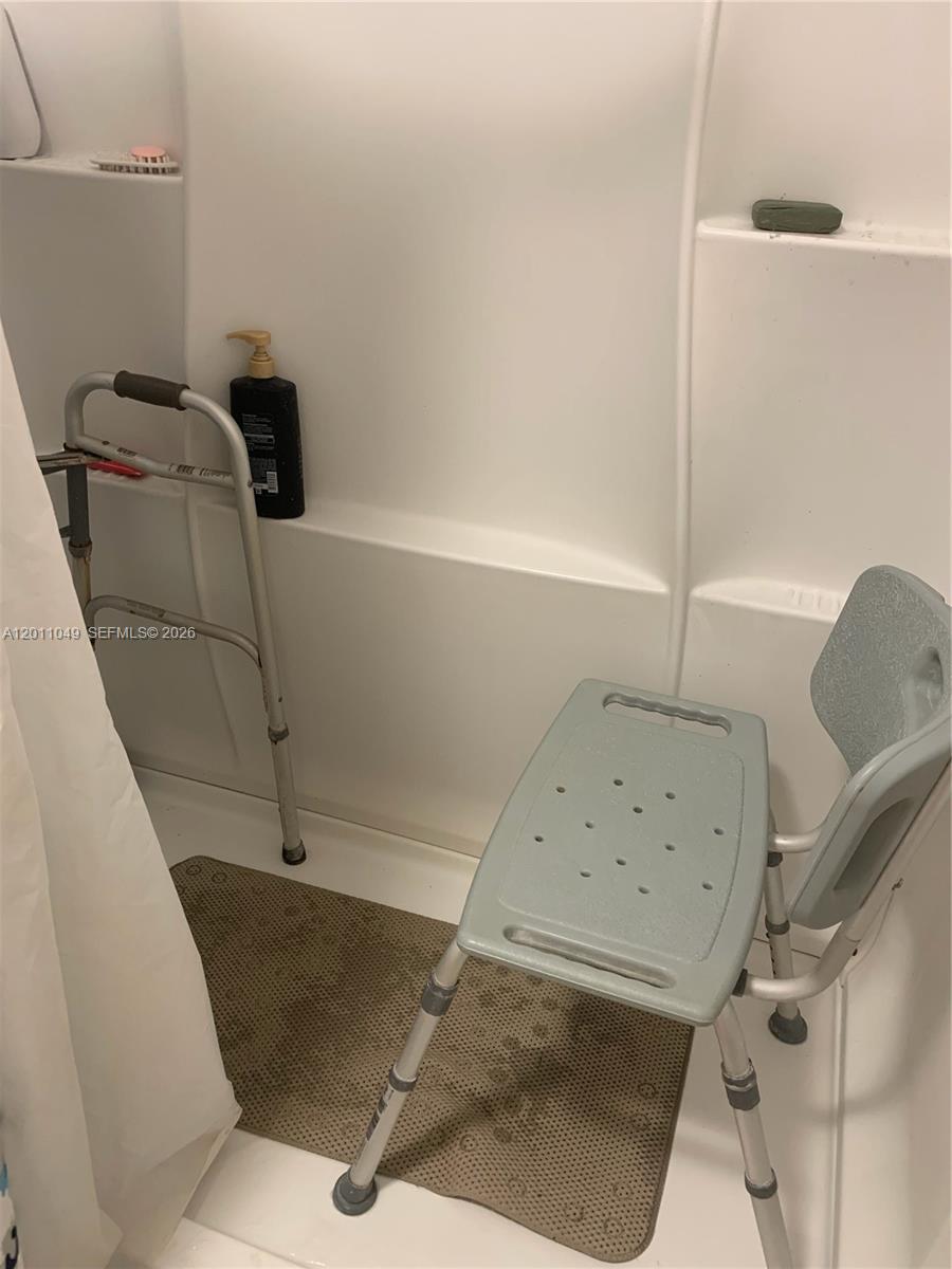 A shower stall features a gray shower chair and a metal walker inside — 1495 SW 131st AVE, Miami FL 33184, MIAMI, FL