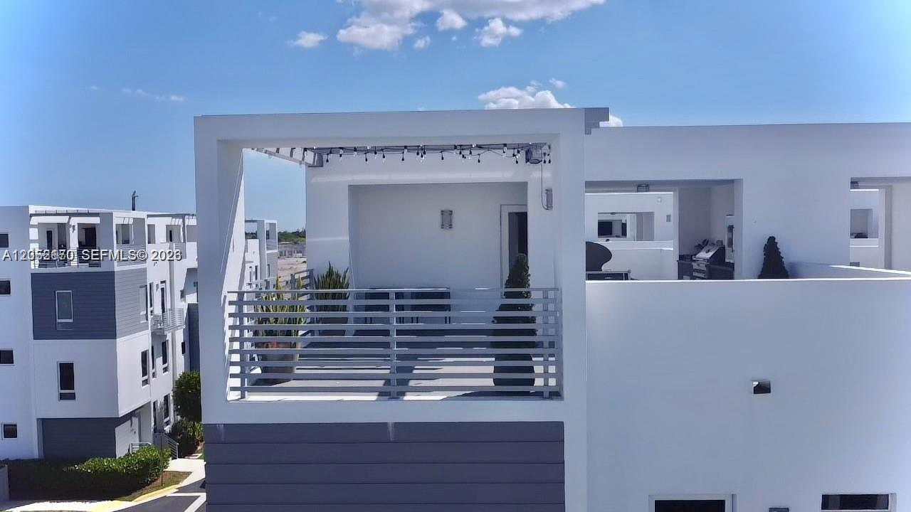 A modern white rooftop terrace features a metal railing and string lights under a blue sky — 9151 NW 33rd St, Doral FL 33172, DORAL, FL
