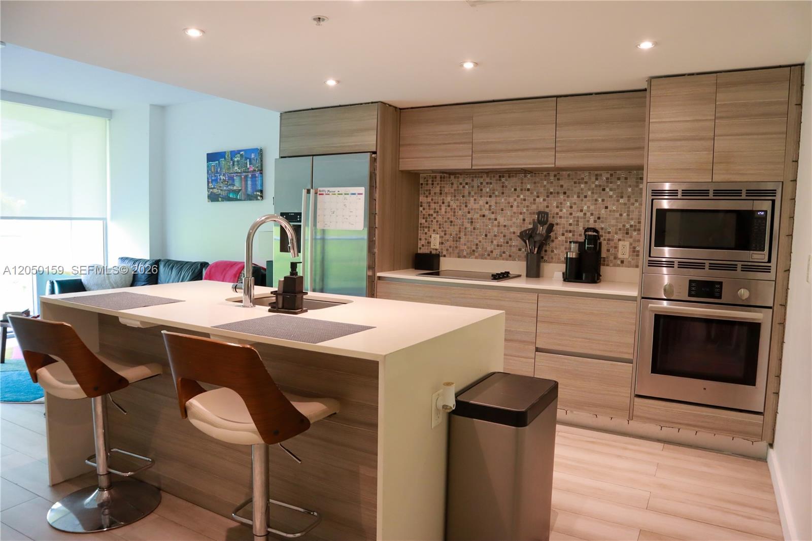 A modern kitchen features wood-grain cabinetry, a central island with bar seating, and stainless appliances — 6620 Indian Creek Dr # 302, Miami Beach FL 33141, MIAMI BEACH, FL