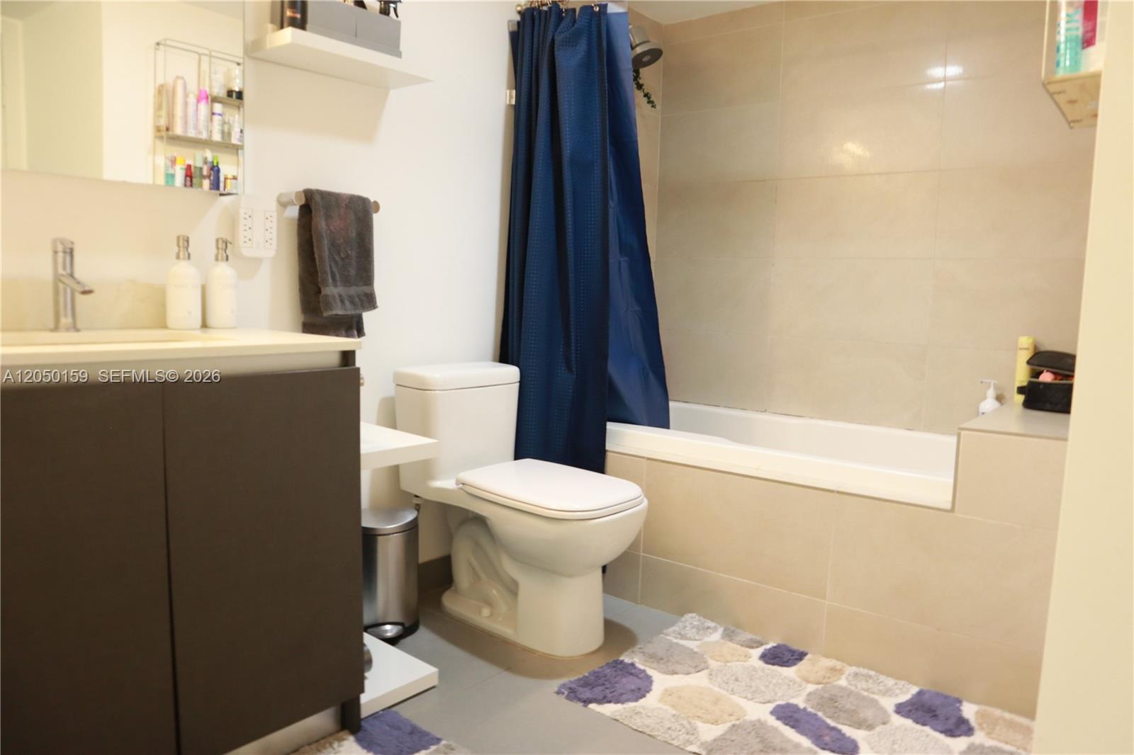 A bathroom features a dark vanity, a toilet, and a bathtub with a blue curtain — 6620 Indian Creek Dr # 302, Miami Beach FL 33141, MIAMI BEACH, FL