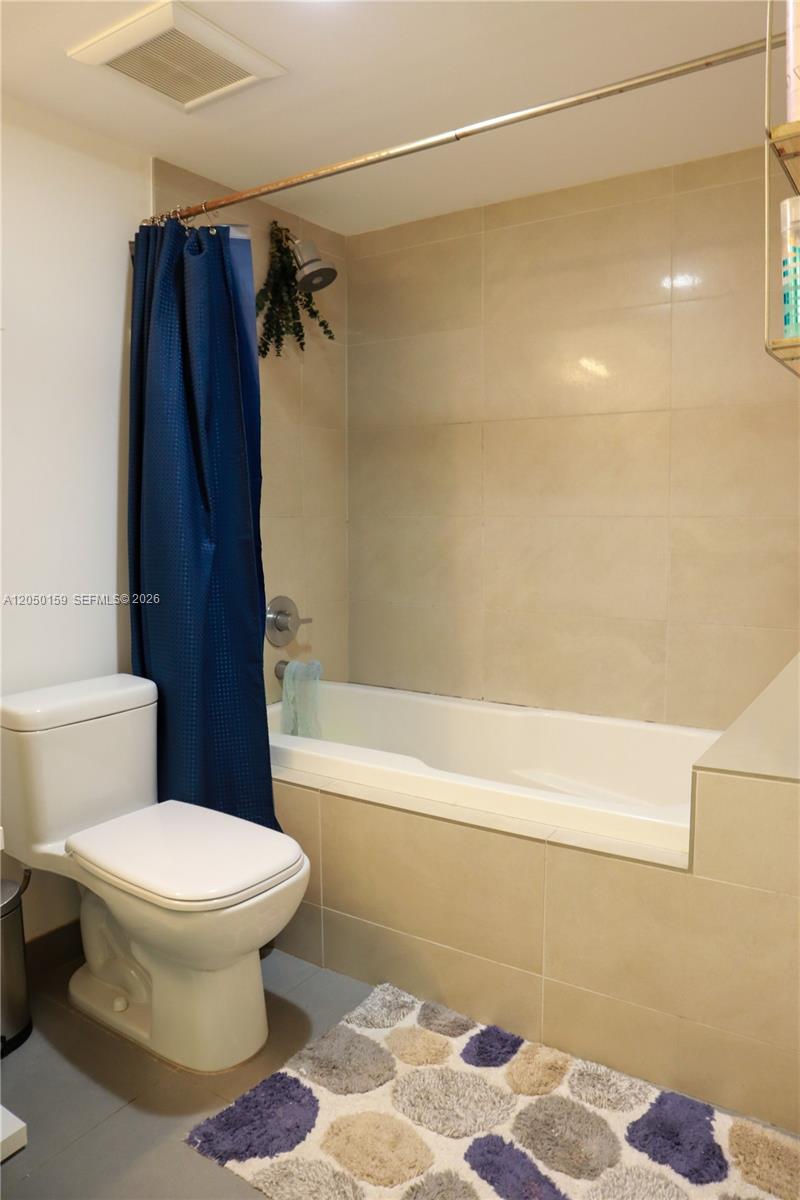 A bathroom features a white toilet, a bathtub with beige tile walls, and a shower — 6620 Indian Creek Dr # 302, Miami Beach FL 33141, MIAMI BEACH, FL