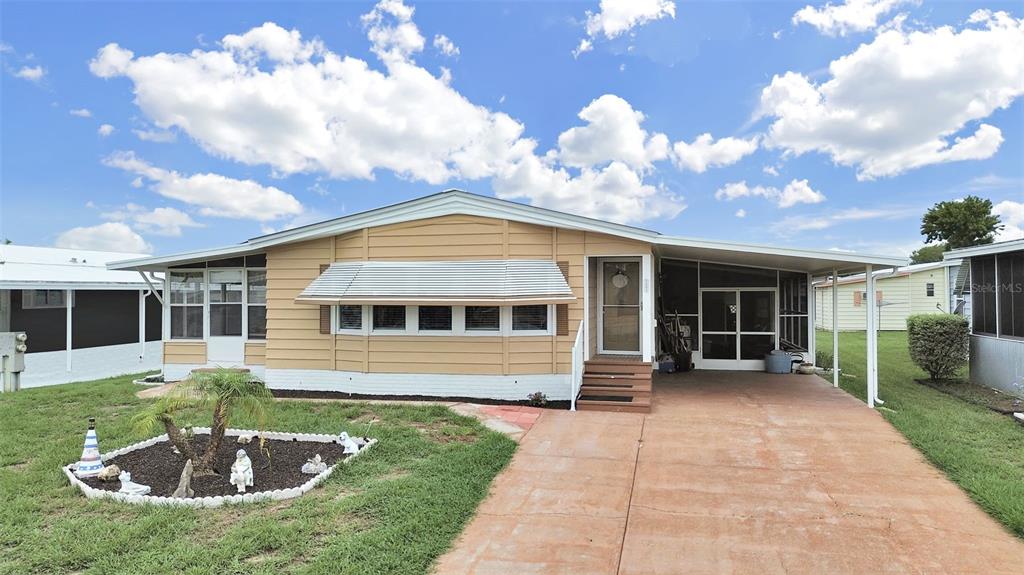A single-story tan mobile home with a carport, front awning, and a small landscaped garden — 5083 LODGEWOOD DR, LAKELAND, FL