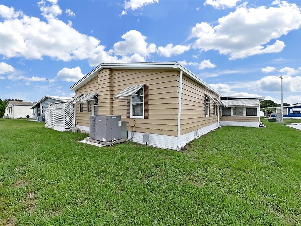 The exterior of a tan mobile home features a central air conditioning unit and white skirting — 5083 LODGEWOOD DR, LAKELAND, FL
