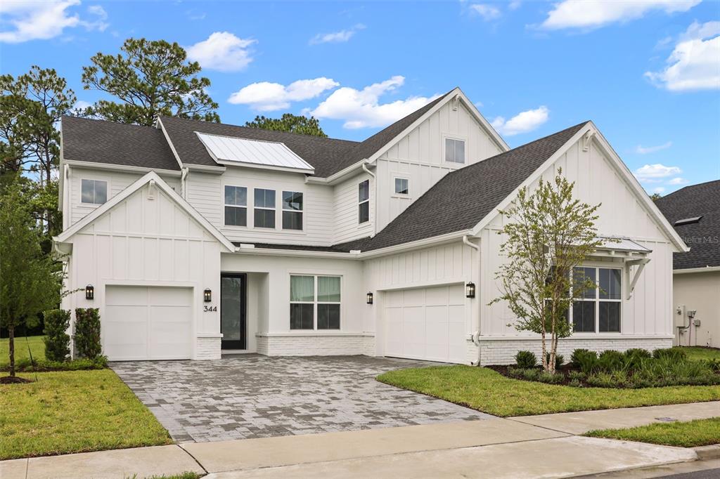 A two-story white farmhouse-style home features a paved driveway, two garages, and dark shingled roofs — 344 AMBERSWEET PLACE, LAKE MARY, FL