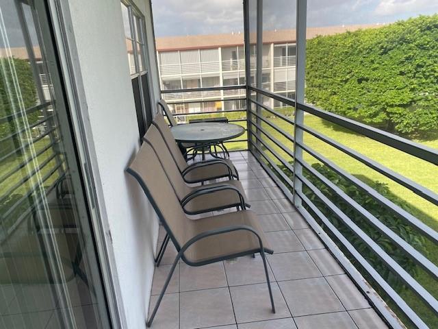 A screened-in balcony features tiled flooring, a small round table, and three patio chairs — 117 Brighton C # 117, Boca Raton FL 33434, BOCA RATON, FL