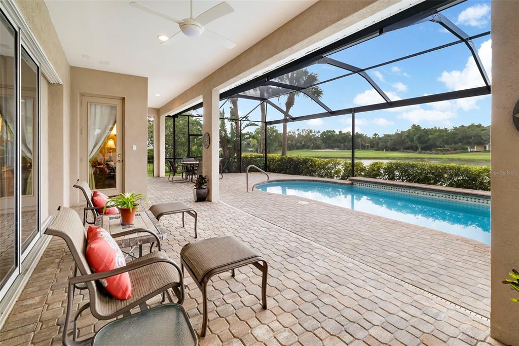 A covered patio with brick pavers features a swimming pool and a view of a golf course — 10625 RESTORATION TERRACE, BRADENTON, FL