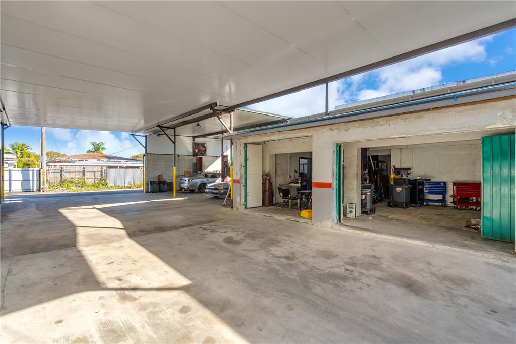 A large concrete-floored covered outdoor workspace with adjacent garage bays and parked vehicles — 3219 SW 8TH STREET, MIAMI, FL