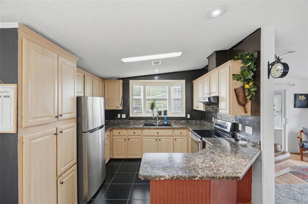 A kitchen features light wood cabinets, dark countertops, black tile flooring, and a stainless refrigerator — 6907 AMERICANA DRIVE NE UNIT 101, ST PETERSBURG, FL
