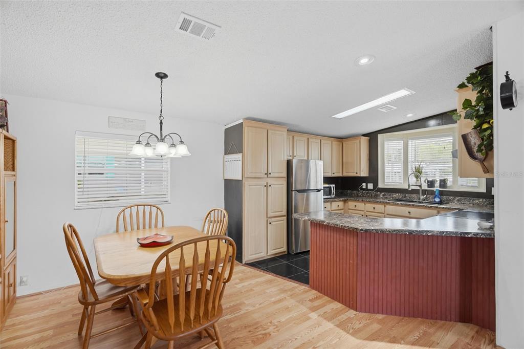 A kitchen and dining area with light wood cabinets, laminate countertops, and wood-look flooring — 6907 AMERICANA DRIVE NE UNIT 101, ST PETERSBURG, FL