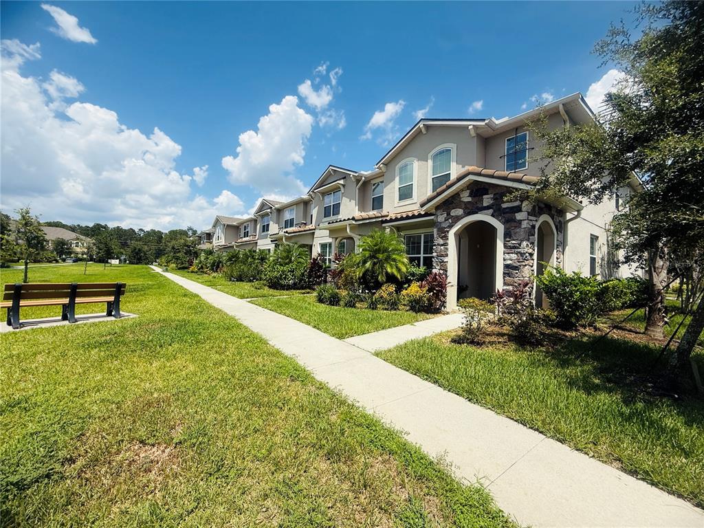 A row of multi-story townhomes with stone accents sits beside a sidewalk and grassy park — 8878 HERENCIA ALLEY, WINDERMERE, FL