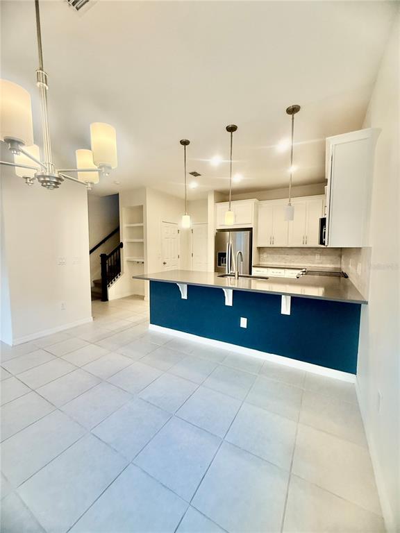 A kitchen features a blue island, white cabinets, stainless steel appliances, and light tile flooring — 8878 HERENCIA ALLEY, WINDERMERE, FL